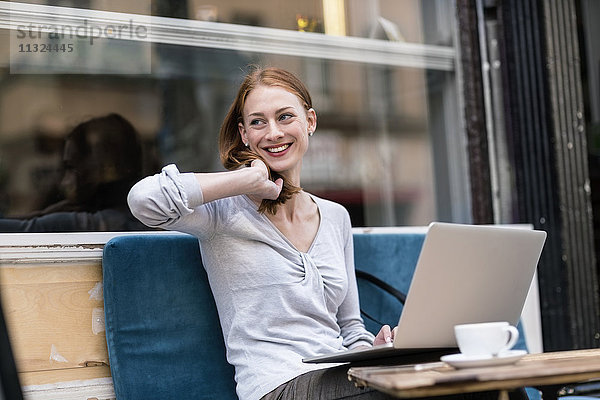 Lächelnde rothaarige Frau mit Laptop im Straßencafé