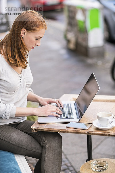 Redheaded Frau mit Laptop auf dem Bürgersteig Cafe