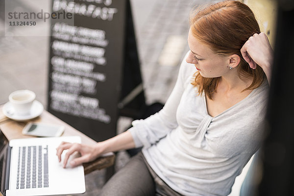 Redheaded Frau mit Laptop auf dem Bürgersteig Cafe