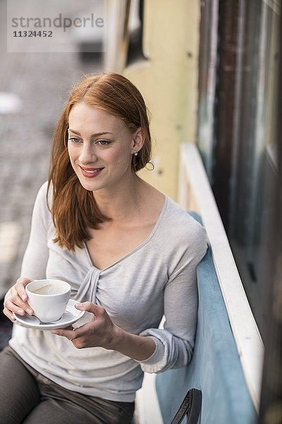 Rothaarige Frau trinkt Kaffee im Straßencafé
