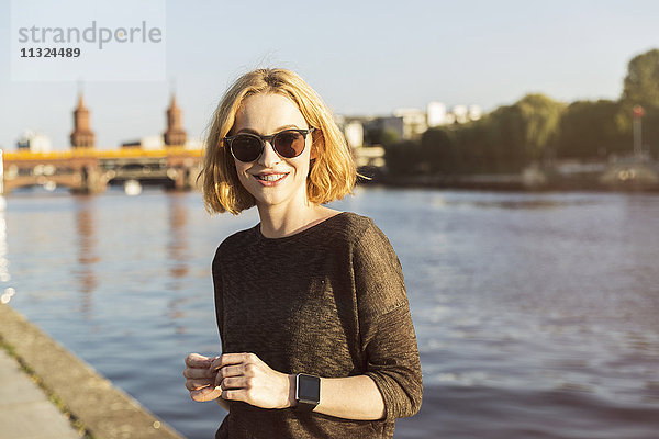 Deutschland  Berlin  Portrait einer lächelnden jungen Frau mit Sonnenbrille und Smartwatch