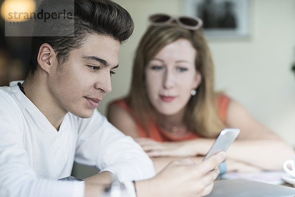 Teenager-Junge mit Handy und Frau im Hintergrund