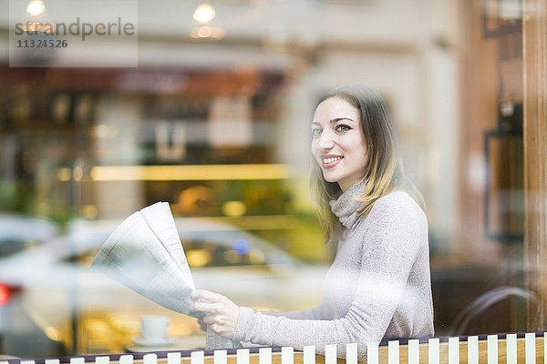 Junge Frau sitzt im Café und liest Zeitung.
