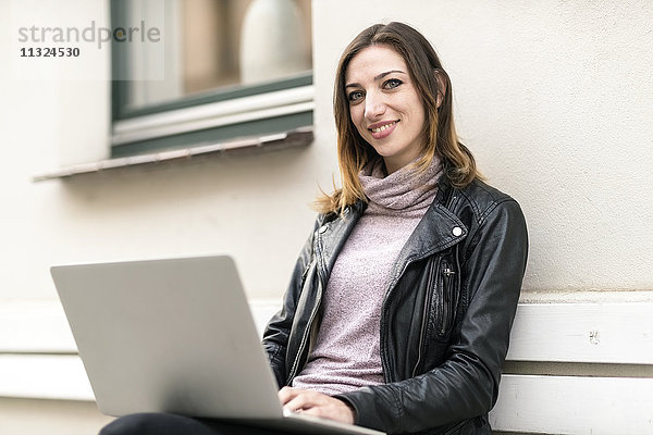 Junge Frau sitzend auf der Außenbank mit Laptop