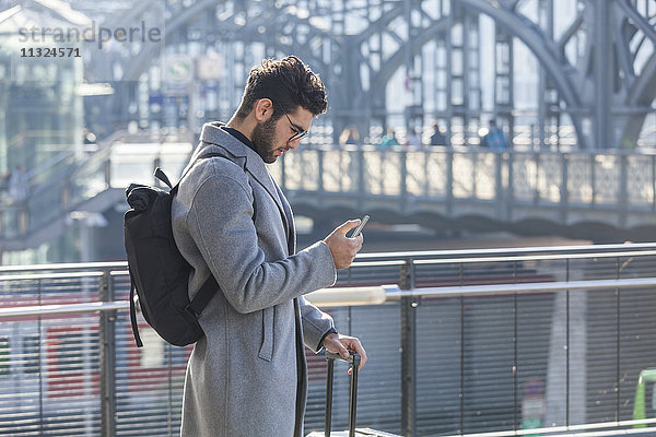 Geschäftsmann mit Gepäck beim Blick aufs Handy am Bahnhof