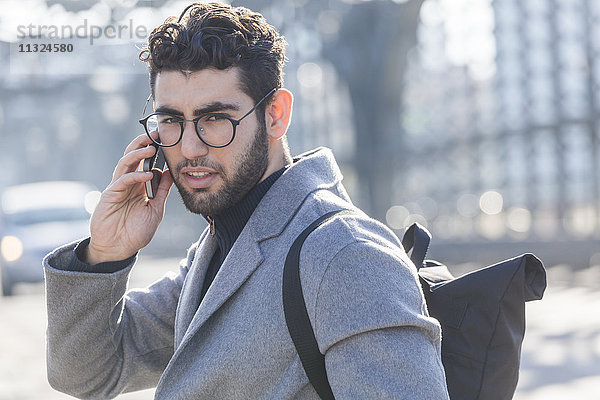 Portrait eines jungen Geschäftsmannes mit Rucksack am Telefon