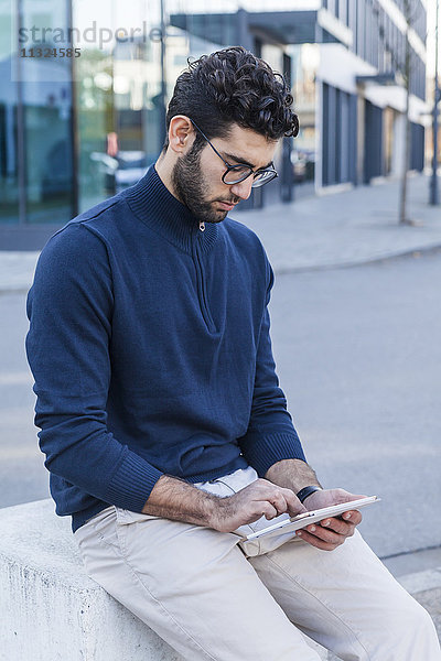 Junger Mann sitzend auf Poller mit Mini-Tablette