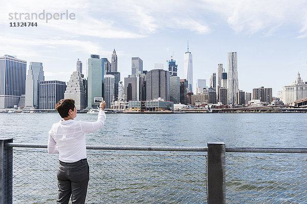 USA  Brooklyn  Geschäftsfrau beim Fotografieren der Skyline von Manhattan