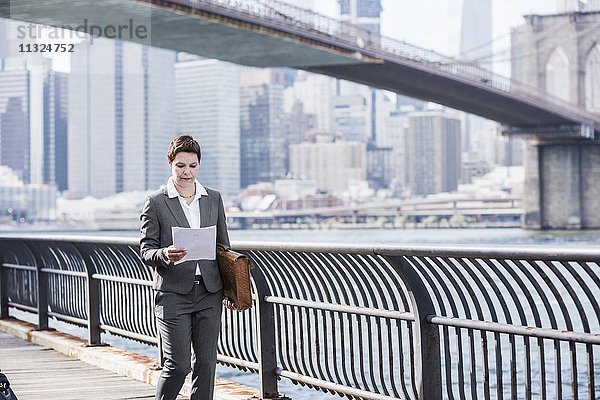 USA  Brooklyn  Geschäftsfrau beim Lesen von Zeitungen vor den Wolkenkratzern von Manhattan