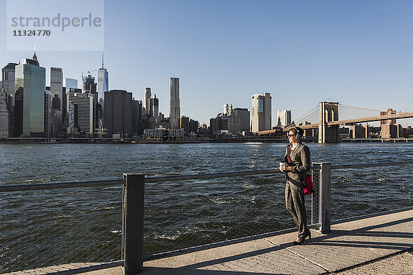 USA  Brooklyn  Geschäftsfrau mit Kopfhörer mit Blick auf die Skyline von Manhattan