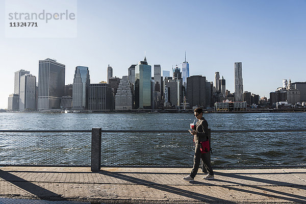 USA  Brooklyn  Geschäftsfrau mit Blick auf ihr Smartphone vor der Skyline von Manhattan