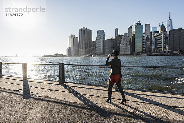 USA  Brooklyn  Geschäftsfrau beim Kaffeetrinken vor der Skyline von Manhattan