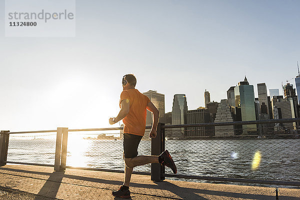 USA  Brooklyn  Mann joggen vor der Skyline von Manhattan am Abend