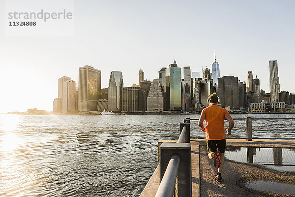 USA  Brooklyn  Rückansicht des Mannes  der abends vor der Skyline von Manhattan joggt.
