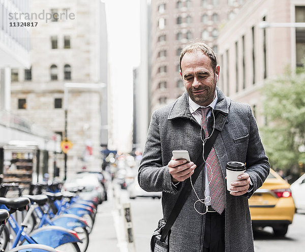 USA  New York City  Geschäftsmann unterwegs in Manhattan mit Blick aufs Handy