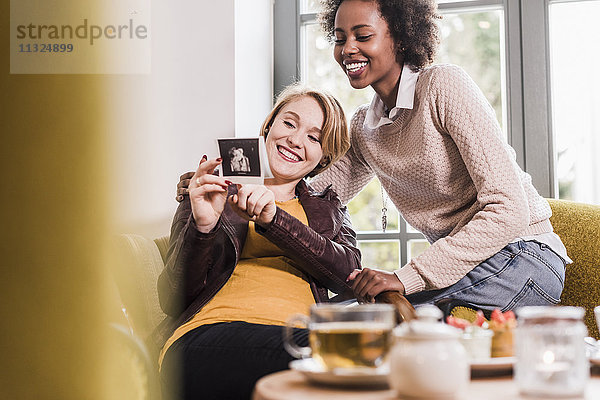Eine schwangere junge Frau zeigt einem Freund in einem Café einen Ultraschall.