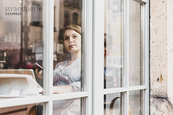 Junge Frau mit Tablette und Handy in einem Café mit Blick aus dem Fenster