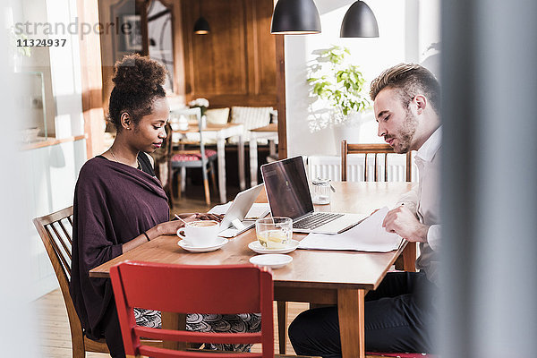 Junger Mann und Frau mit Laptop und Tablett in einem Cafe
