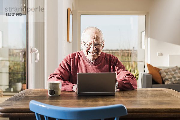 Senior Mann sitzt zu Hause  mit Laptop