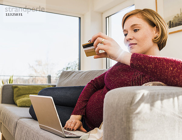 Schwangere Frau auf der Couch online einkaufen