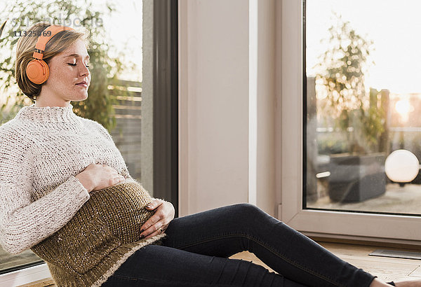 Eine schwangere Frau sitzt auf dem Boden und hört Musik.