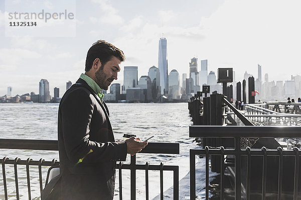 USA  Geschäftsmann mit Handy am New Jersey Waterfront mit Blick auf Manhattan
