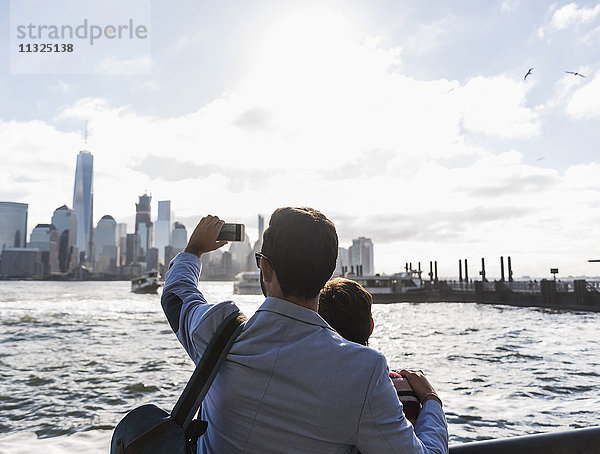 USA  Mann und Frau an der New Jersey Waterfront mit Blick auf Manhattan beim Fotografieren von Mobiltelefonen