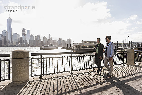 USA  zwei Geschäftsleute  die an der Waterfront von New Jersey mit Blick auf Manhattan spazieren gehen.