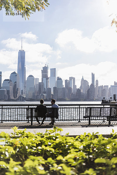 USA  zwei Geschäftsleute sitzen auf einer Bank an der New Jersey Waterfront mit Blick auf Manhattan