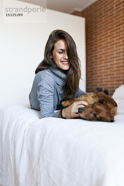 Glückliche junge Frau liegt im Bett und spielt mit ihrem Hund.