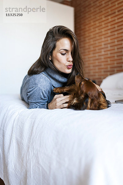 Junge Frau liegt im Bett und spielt mit ihrem Hund.