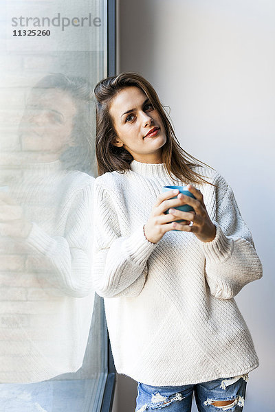 Junge Frau beim Kaffeetrinken am Fenster