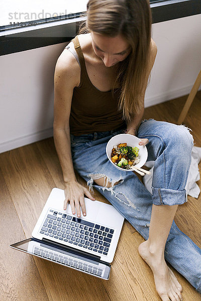 Frau zu Hause essen Gemüse mit Stäbchen und mit dem Laptop