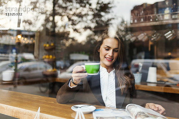 Lächelnde junge Frau in einem Café beim Lesen einer Zeitschrift