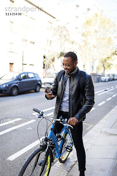 Lächelnder junger Mann mit Fahrrad auf seinem Smartphone