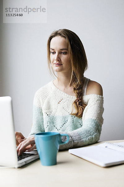 Porträt einer jungen Frau  die zu Hause mit dem Laptop arbeitet