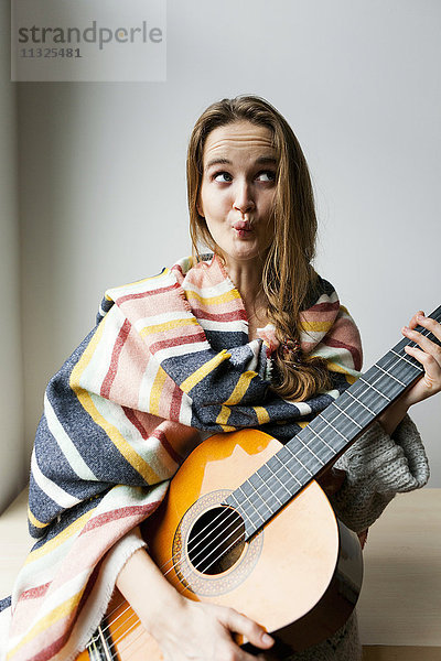Junge Frau mit Decke und Gitarre zieht lustige Gesichter