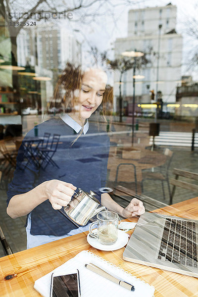 Lächelnde junge Frau mit Laptop und Tasse Tee im Cafe