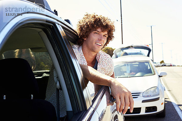 Lächelnder junger Mann schaut aus dem Autofenster.