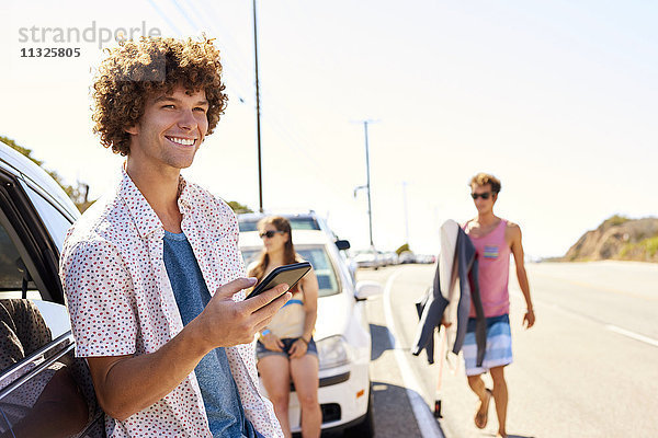 Lächelnder junger Mann an einem Auto mit Handy