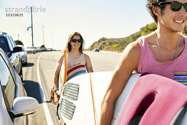 Lächelndes junges Paar mit Surfbrettern auf der Küstenstraße
