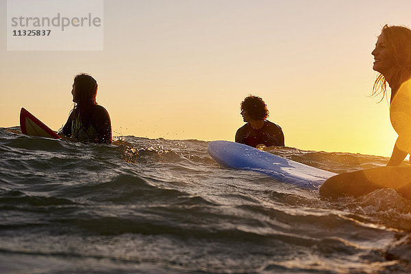 Drei Surfer im Meer bei Sonnenuntergang
