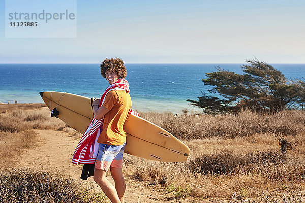 Junger Mann mit Surfbrett an der Küste