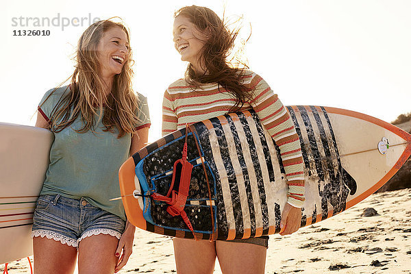 Zwei glückliche Frauen mit Surfbrettern am Strand