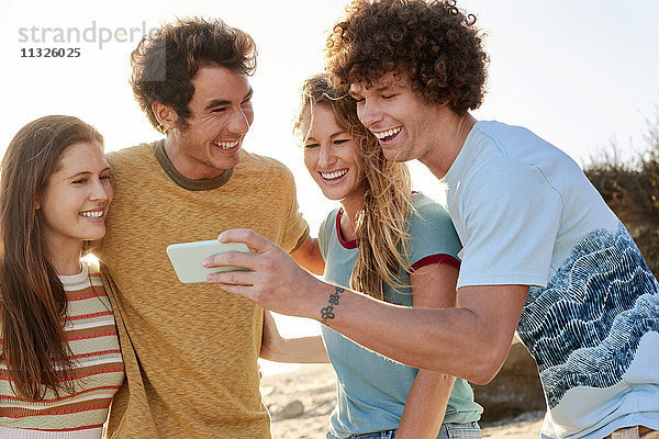 Glückliche Freunde mit Handy am Strand