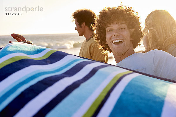 Glücklicher junger Mann mit Handtuch am Strand