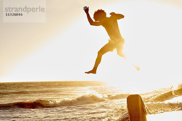 Verspielter Mann beim Springen am Strand bei Sonnenuntergang