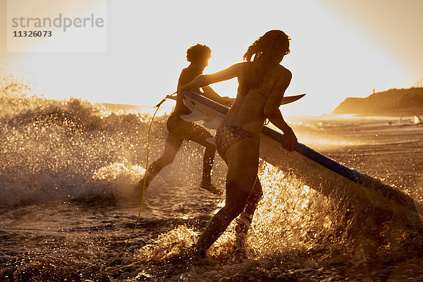Surfer  die bei Sonnenuntergang ins Meer laufen