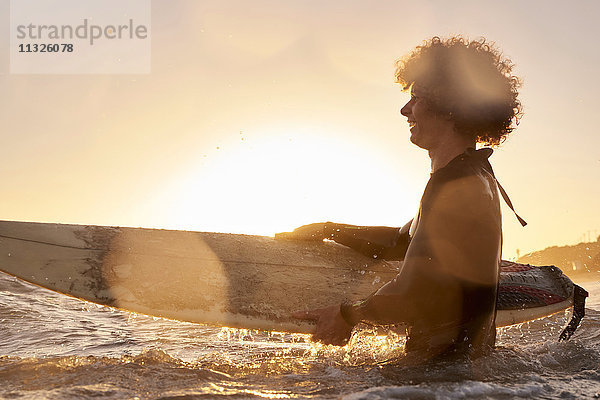 Glücklicher Surfer im Meer bei Sonnenuntergang