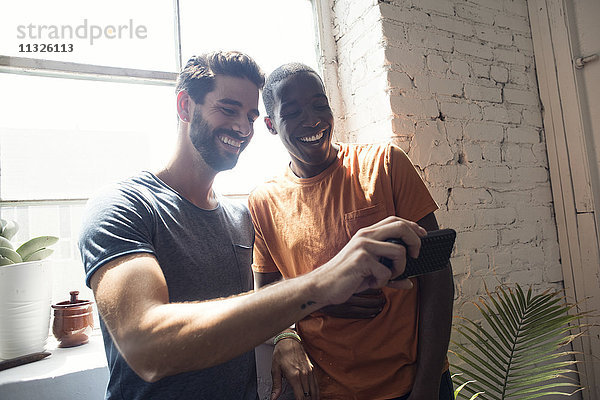 Zwei glückliche junge Männer mit Handy in einem Loft